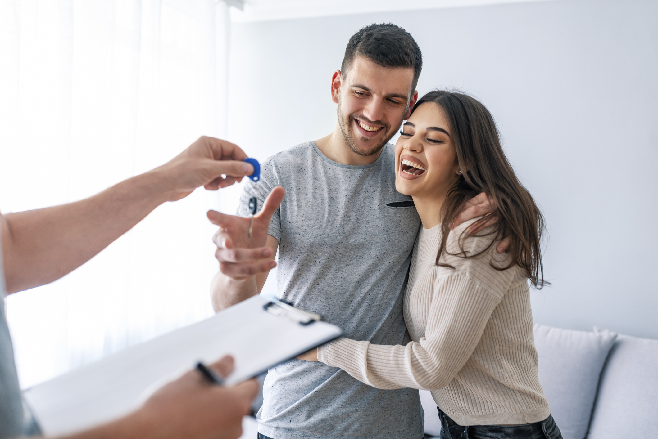 Happy couple is taking keys from their new house from broker and smiling. Happy couple is taking keys from their new house from broker and smiling. Hands of estate agent giving keys to the couple. The agent handed the keys a young couple